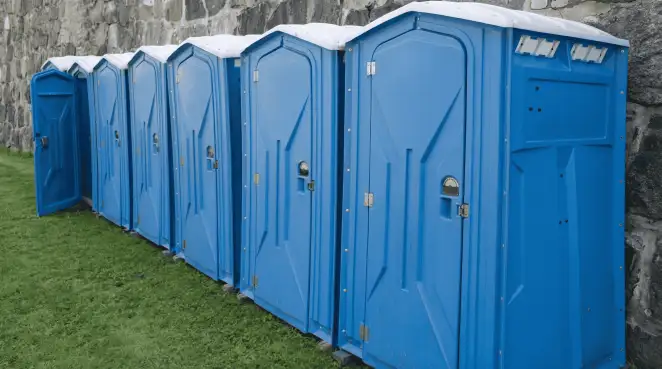 Row of blue portable toilets lined up on grass against a stone wall for event sanitation in Akron, OH