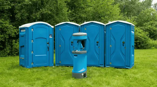 Four blue portable toilets and a matching hand washing station on grass near trees, a common sight at local outdoor events in Akron, OH