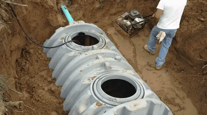 Septic tank installation showing a technician compacting soil around a new poly septic tank in an excavation pit in Akron, OH